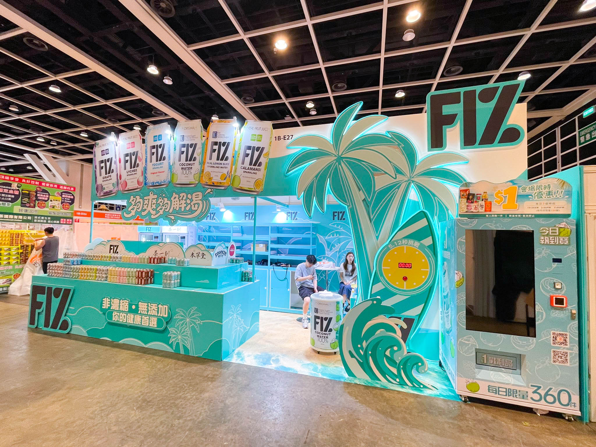 Completed front view of FIZ booth showing product display counter, palm-tree feature, wave floor graphics and vending machine